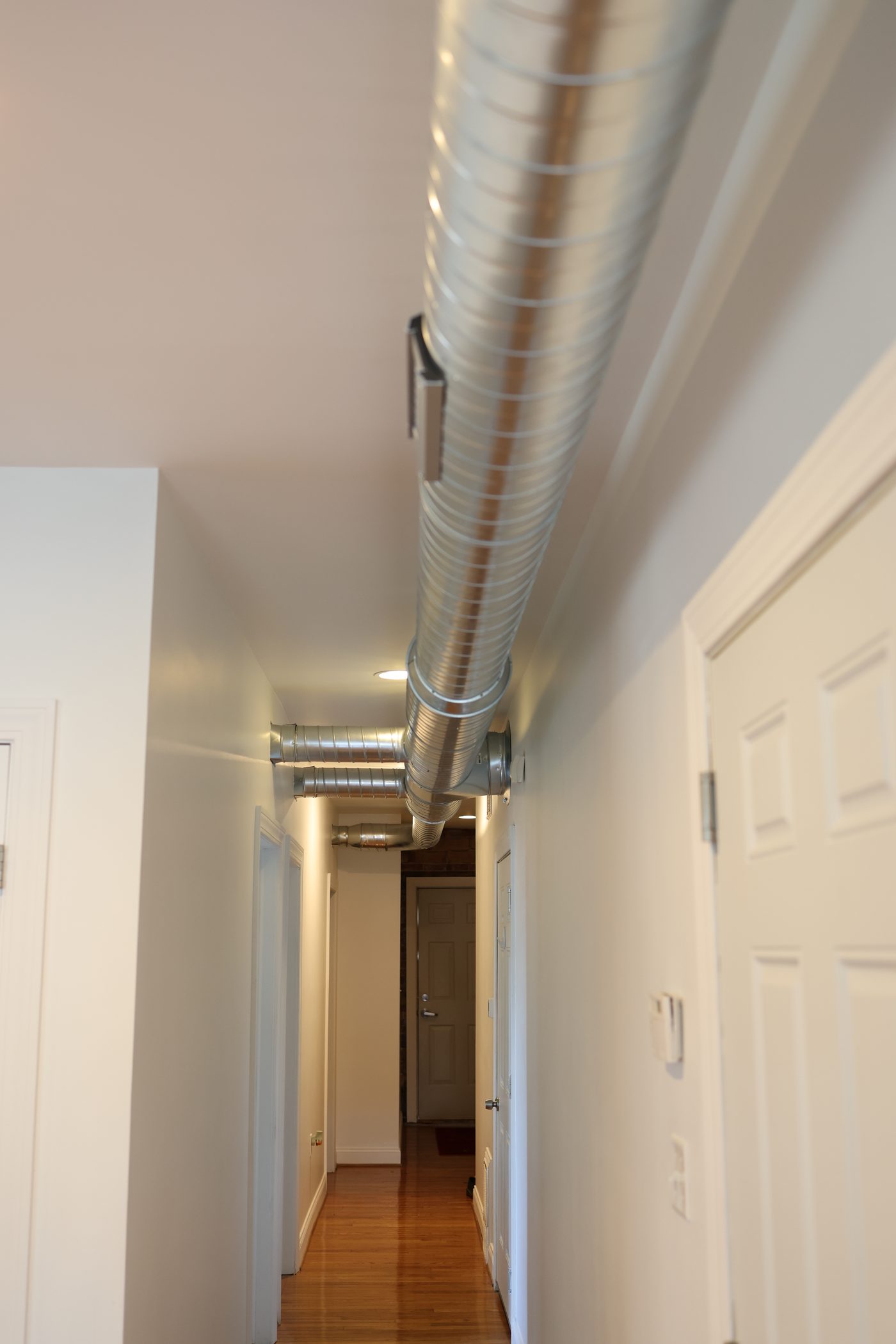 Exposed spiral ductwork running along a finished hallway ceiling