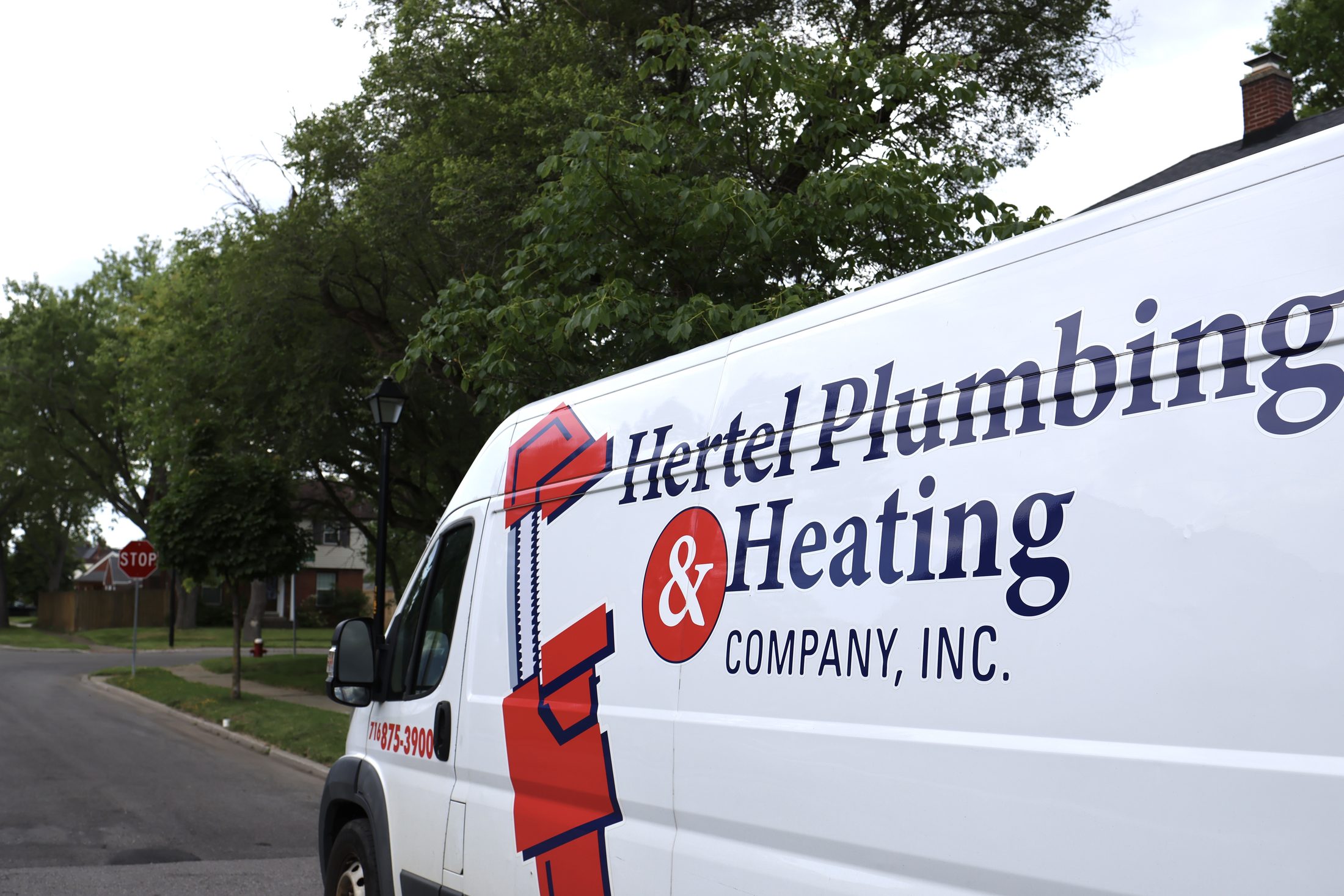 A Hertel Plumbing & Heating service van parked on a tree-lined Buffalo street